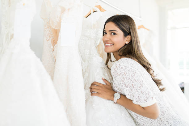 Good looking woman smiling while selecting white wedding dress at boutique