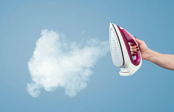 Female hand holds the iron with steam on a blue background